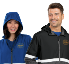 Two people wear TURNABOUT REVERSIBLE JACKETS with hoods and reflective stripes; the woman on the left has a blue jacket with the hood up, while the man on the right wears a black jacket and smiles.