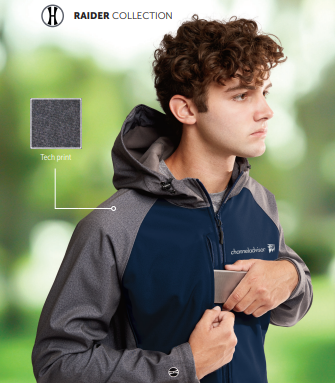 A young man with curly hair wears the RAIDER SOFT SHELL JACKET in two-tone gray and navy, unzipping the chest pocket to reveal a phone. A square highlights the tech print fabric, with blurred green foliage in the background.